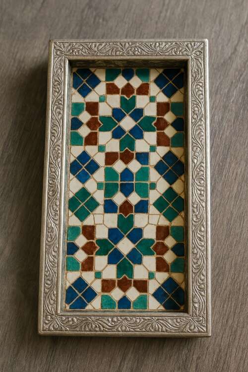Support de stylo rectangulaire en zellige marocain, avec un cadre argenté orné de motifs floraux et une mosaïque colorée de carreaux bleus, verts, marrons et blancs. Posé sur un bureau en bois clair, il mêle artisanat traditionnel et design contemporain.